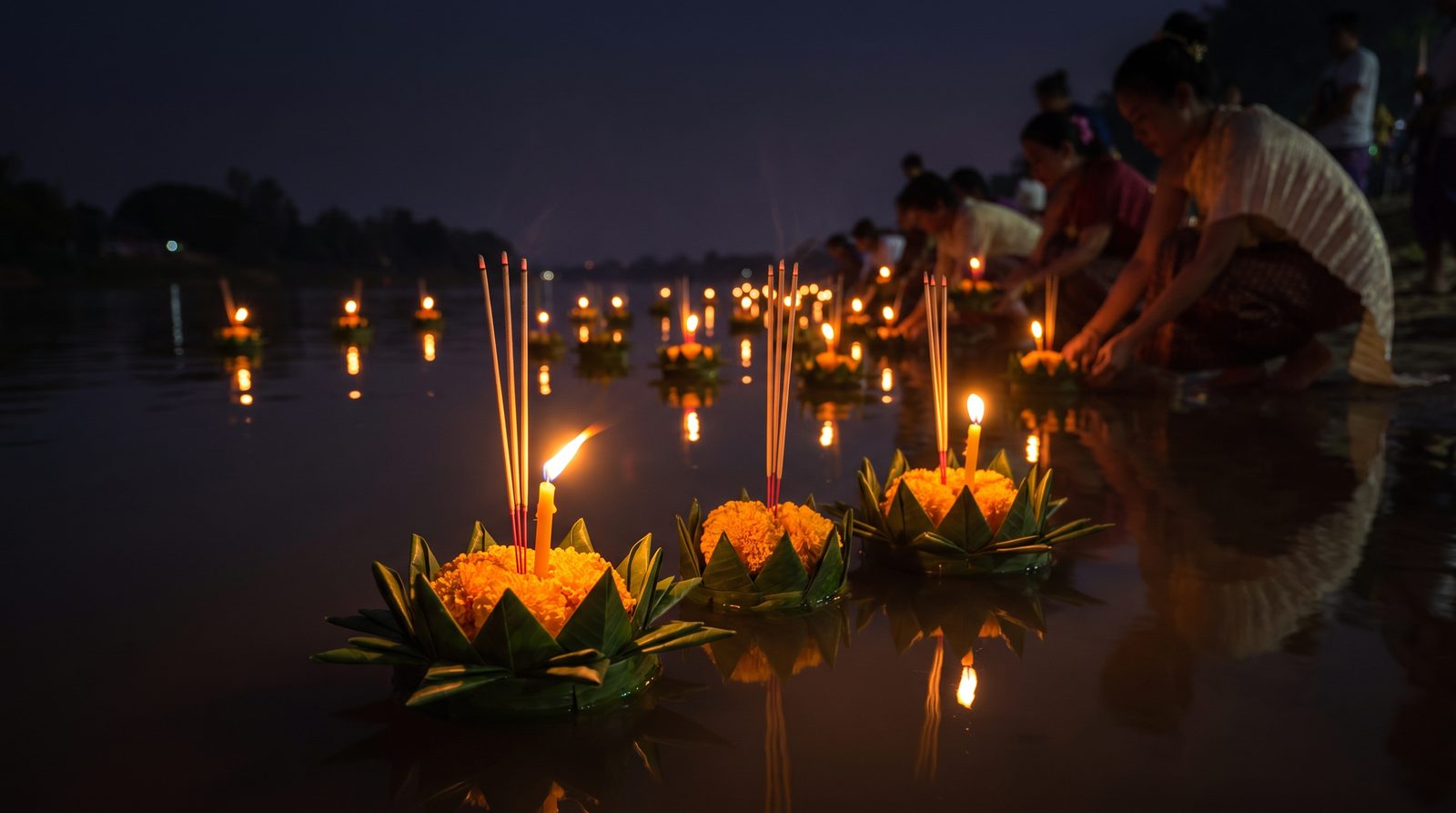 Lit banana-leaf krathong floats with candles and marigolds drifting on dark water during Loi Krathong