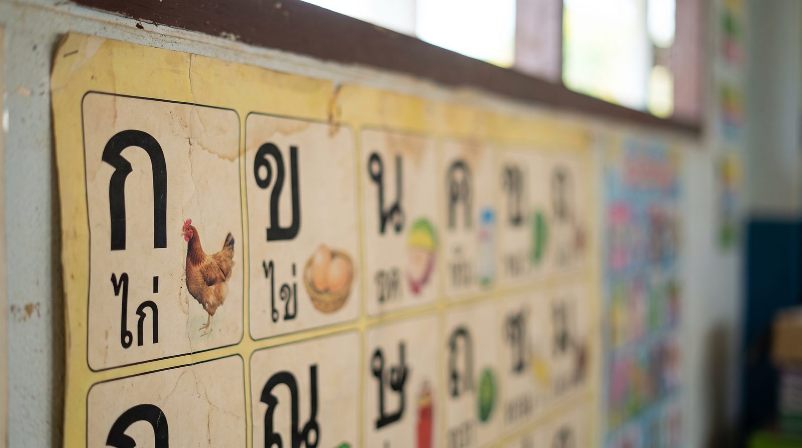 Thai alphabet chart on a classroom wall showing the consonants ko kai and kho khai, used to explain how to read Thai script and where Thai vowels sit
