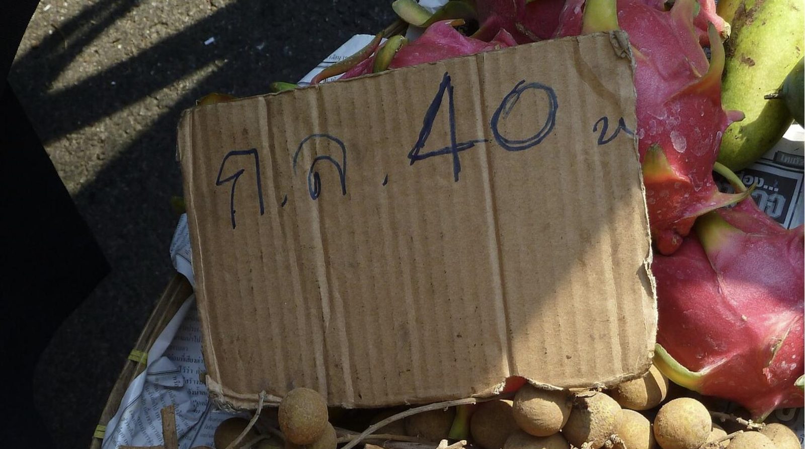 Handwritten Thai price sign reading กก. 40 บ on a Bangkok fruit stall beside longan, dragon fruit and bananas, used to learn Thai vocabulary
