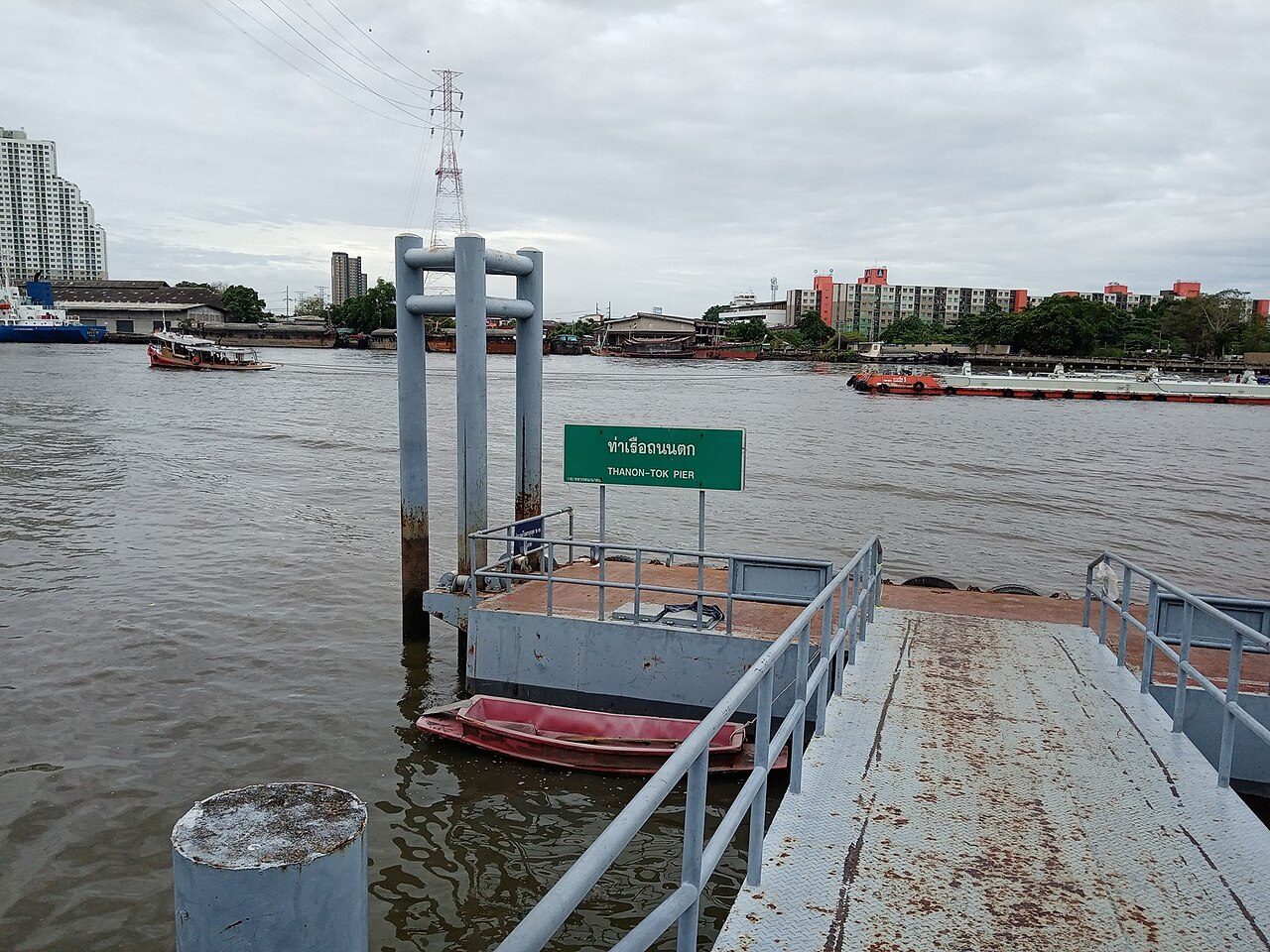 Green Thai pier sign reading ท่าเรือถนนตก with THANON-TOK PIER underneath on the Chao Phraya River in Bangkok