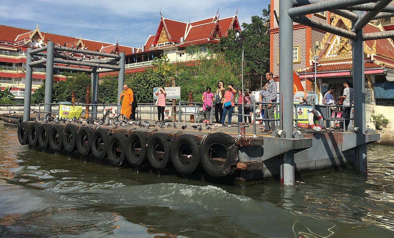 Floating Chao Phraya pier at Wat Soi Thong in Bangkok with a Thai pier sign, car tyres as fenders and passengers waiting to board
