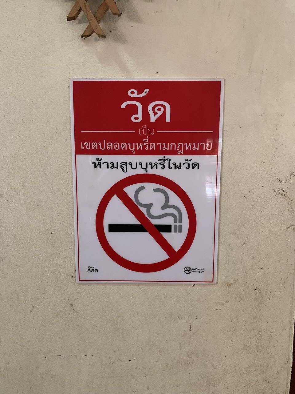 Red and white no-smoking sign in Thai script at a temple in Thailand reading ห้ามสูบบุหรี่ในวัด