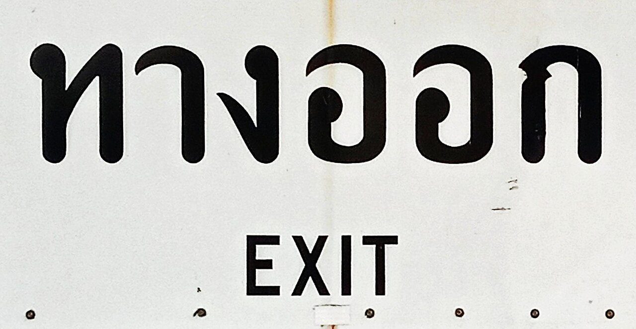 Close-up of a Thai exit sign reading ทางออก in large Thai script with the English word EXIT underneath