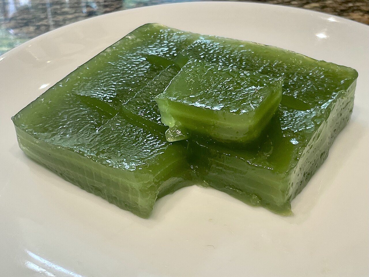 Slice of Thai khanom chan layered pandan jelly dessert on a white plate showing the separate steamed layers at the cut edge