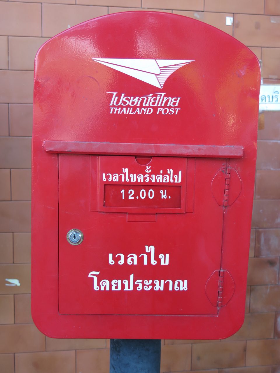 Red Thailand Post postbox in Chiang Rai with Thai script reading next collection time 12.00 and approximate collection time
