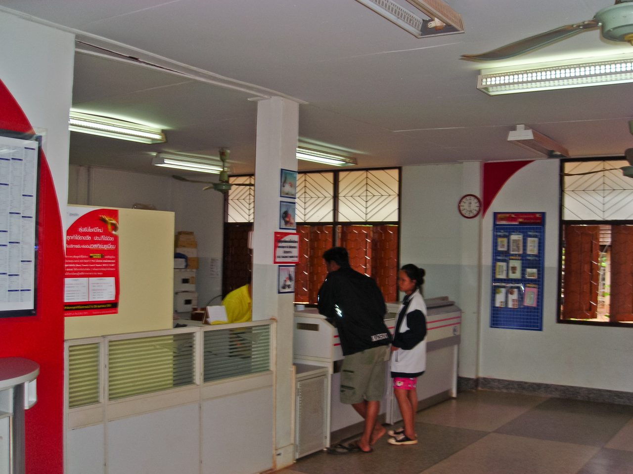 Customers at the counter of a small rural Thai post office in Nakhon Phanom, with Thai-only notices on the walls