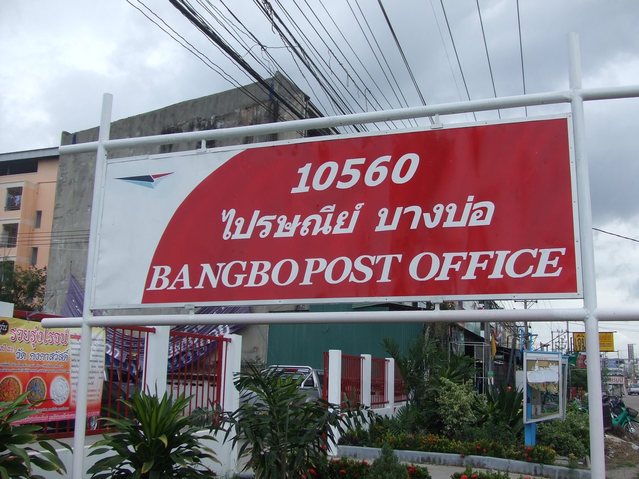 Thai post office sign in Bang Bo, Samut Prakan, reading praisani in Thai script above the English Bangbo Post Office and the postcode 10560