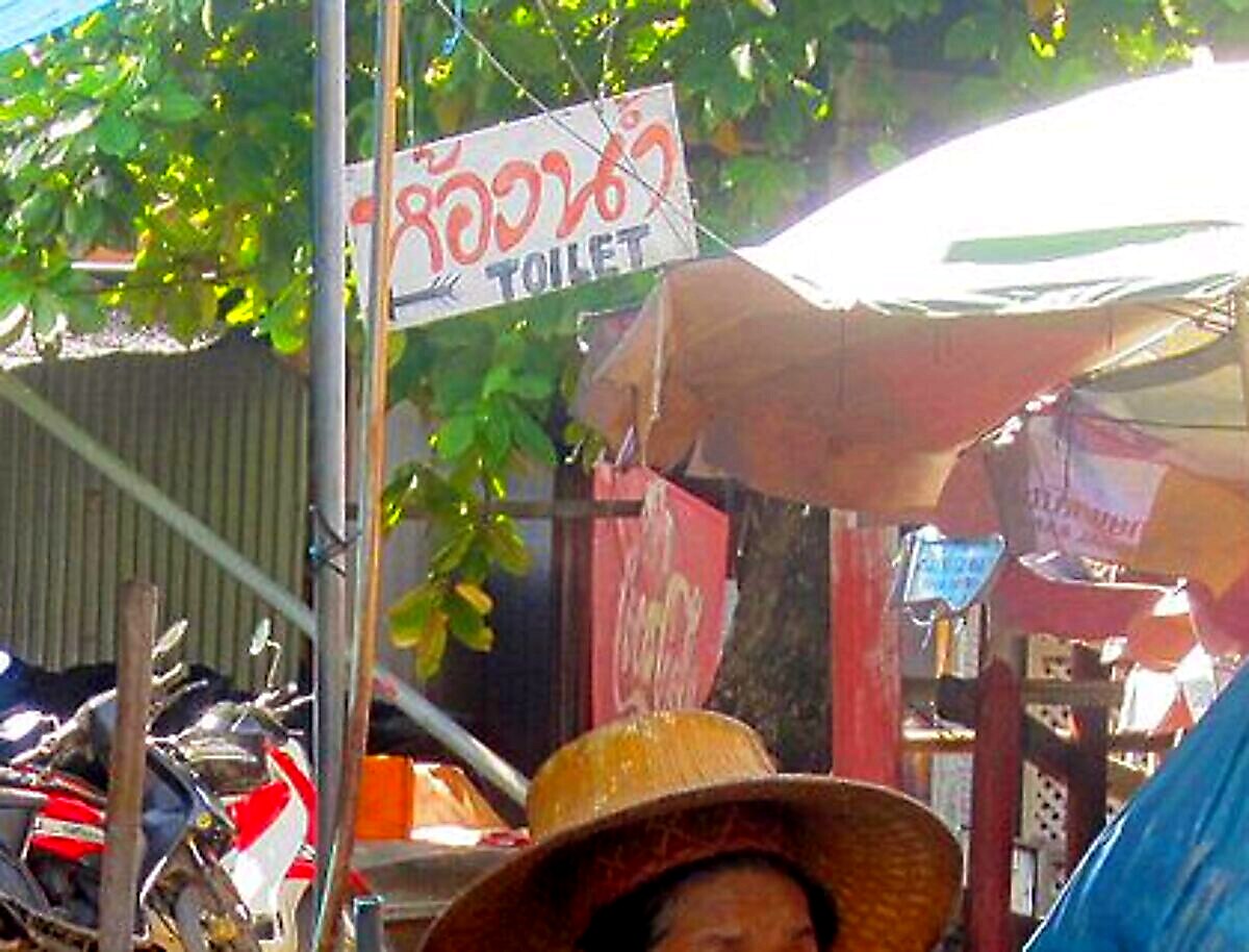 Hand-painted Thai sign reading hong nam above the English word TOILET with an arrow at Damnoen Saduak floating market
