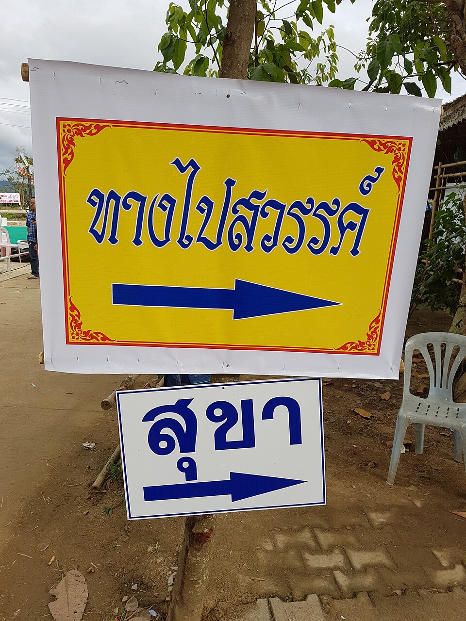 Two Thai signs at a temple in Chiang Rai, one reading thang bpai sawan and one reading sukha with arrows