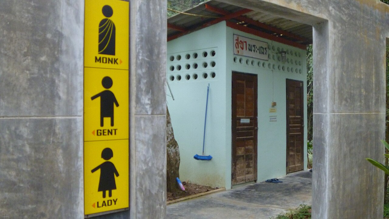Thai temple toilet block with a yellow MONK GENT LADY sign and Thai script reading sukha phra-nen above the doors