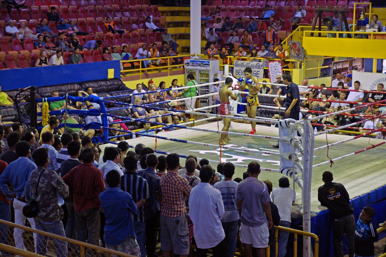 Muay Thai bout at a provincial stadium in Ao Nang Krabi with a standing crowd, referee and a Thai beverage sign