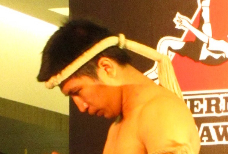 Muay Thai fighter lowering the woven mongkhon headband onto his head before the wai khru ram muay ritual