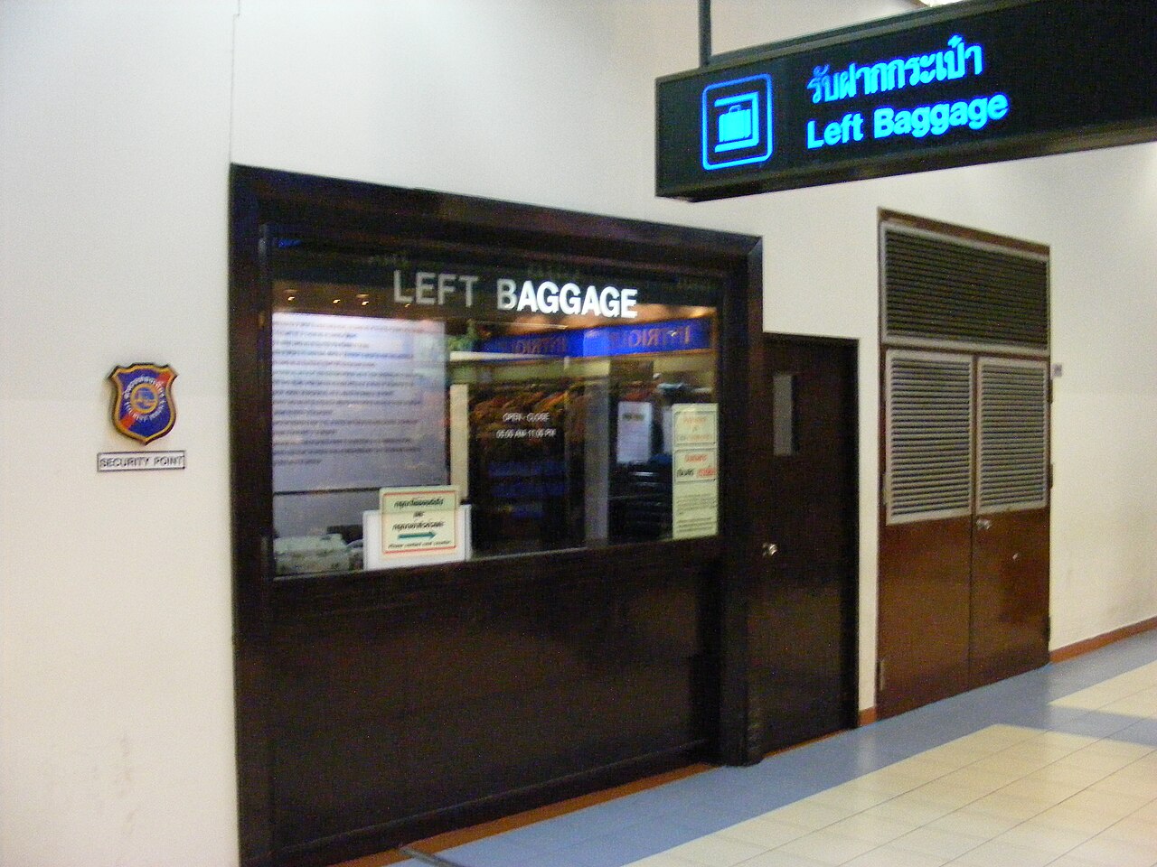 Illuminated Thai letters reading rap faak kra-pao above an English Left Baggage counter sign at Don Mueang Airport in Thailand