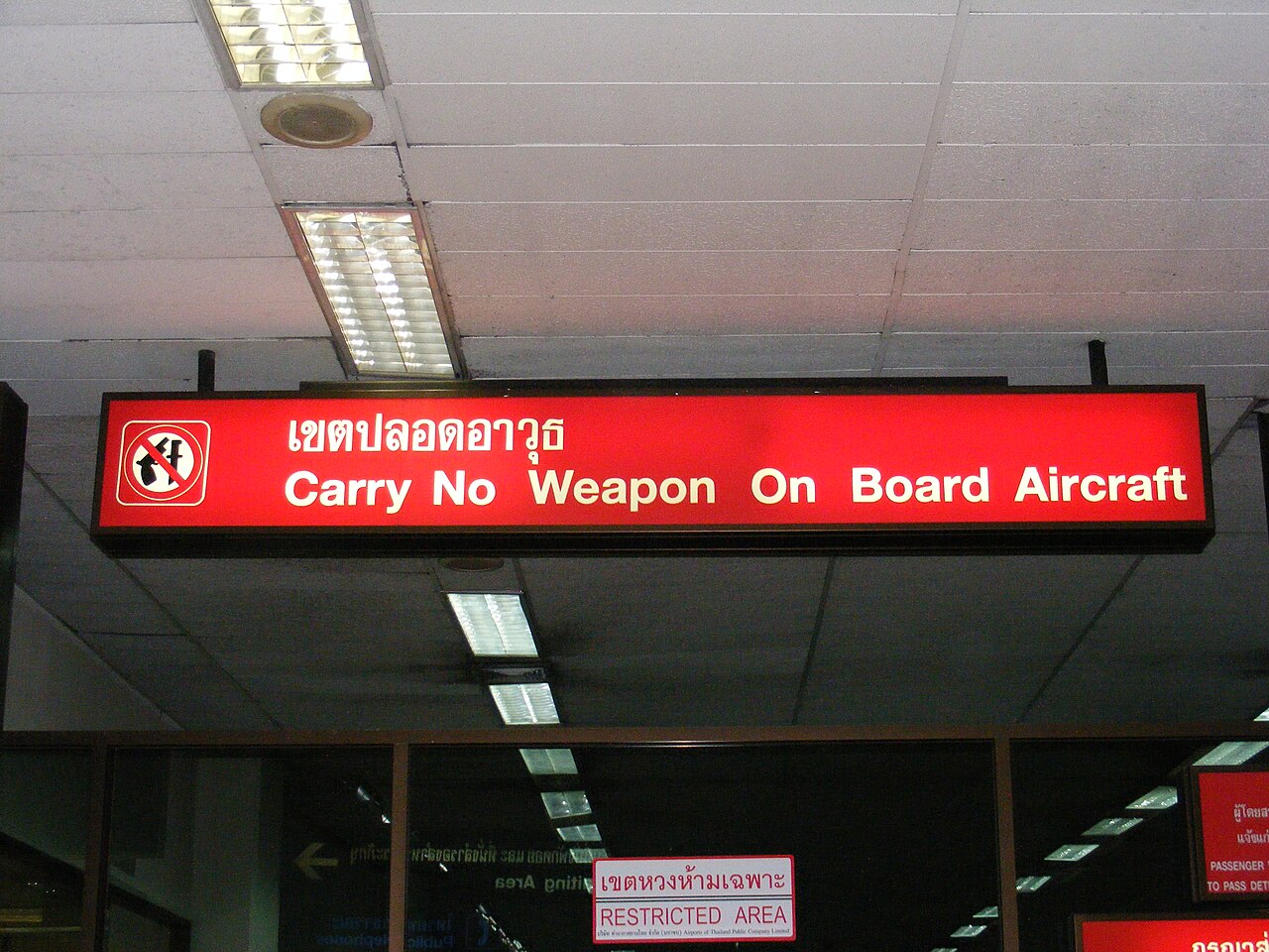 Red Thai airport warning sign reading khet bplawt aa-wut with the English Carry No Weapon On Board Aircraft at Don Mueang Bangkok