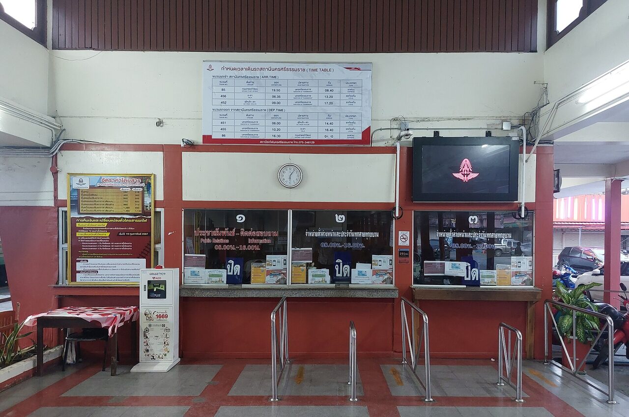 Ticket windows and Thai timetable board inside Nakhon Si Thammarat railway station Thailand with Thai numerals and closed signs in Thai script
