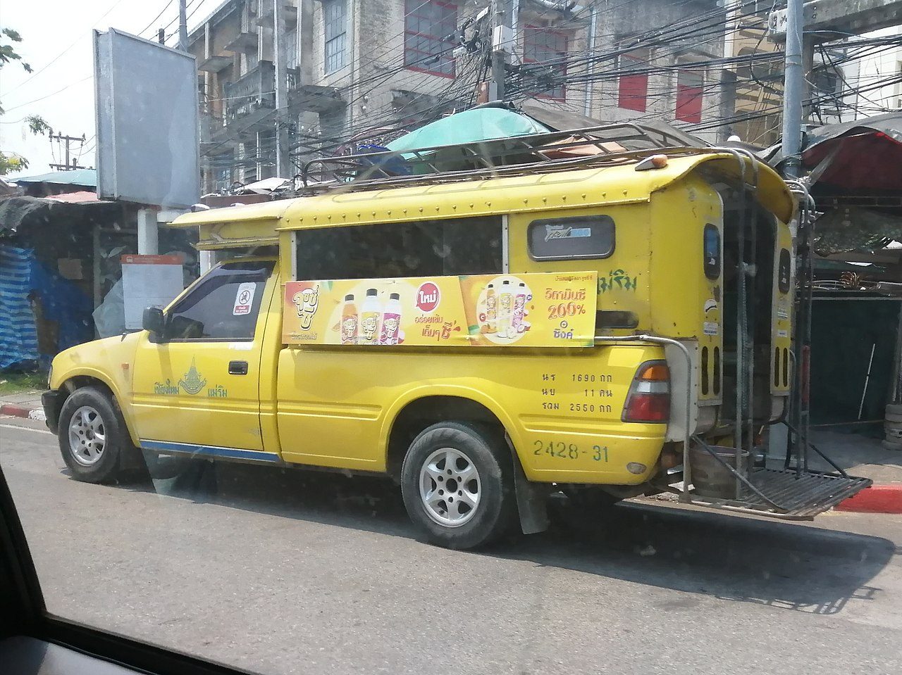 Yellow songthaew shared pickup truck in Chiang Mai Thailand with the route Chiang Mai to Mae Rim painted on the door in Thai script