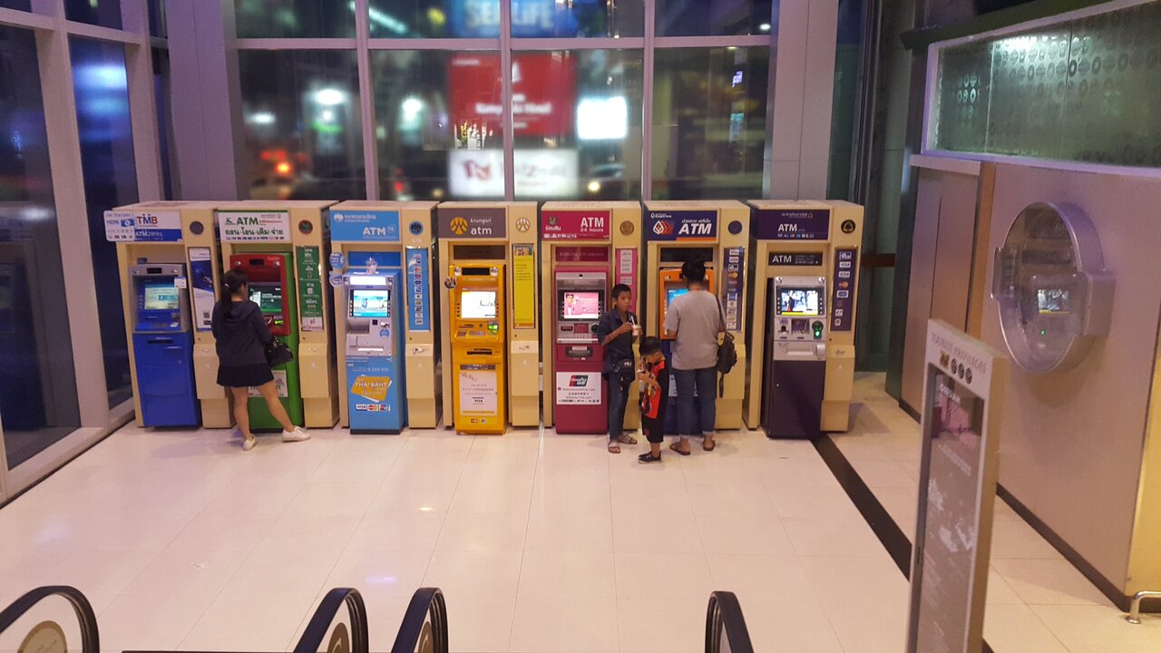 Row of Thai bank ATMs inside Siam Paragon Bangkok with a green Kasikorn machine showing the Thai words thon on toem jai