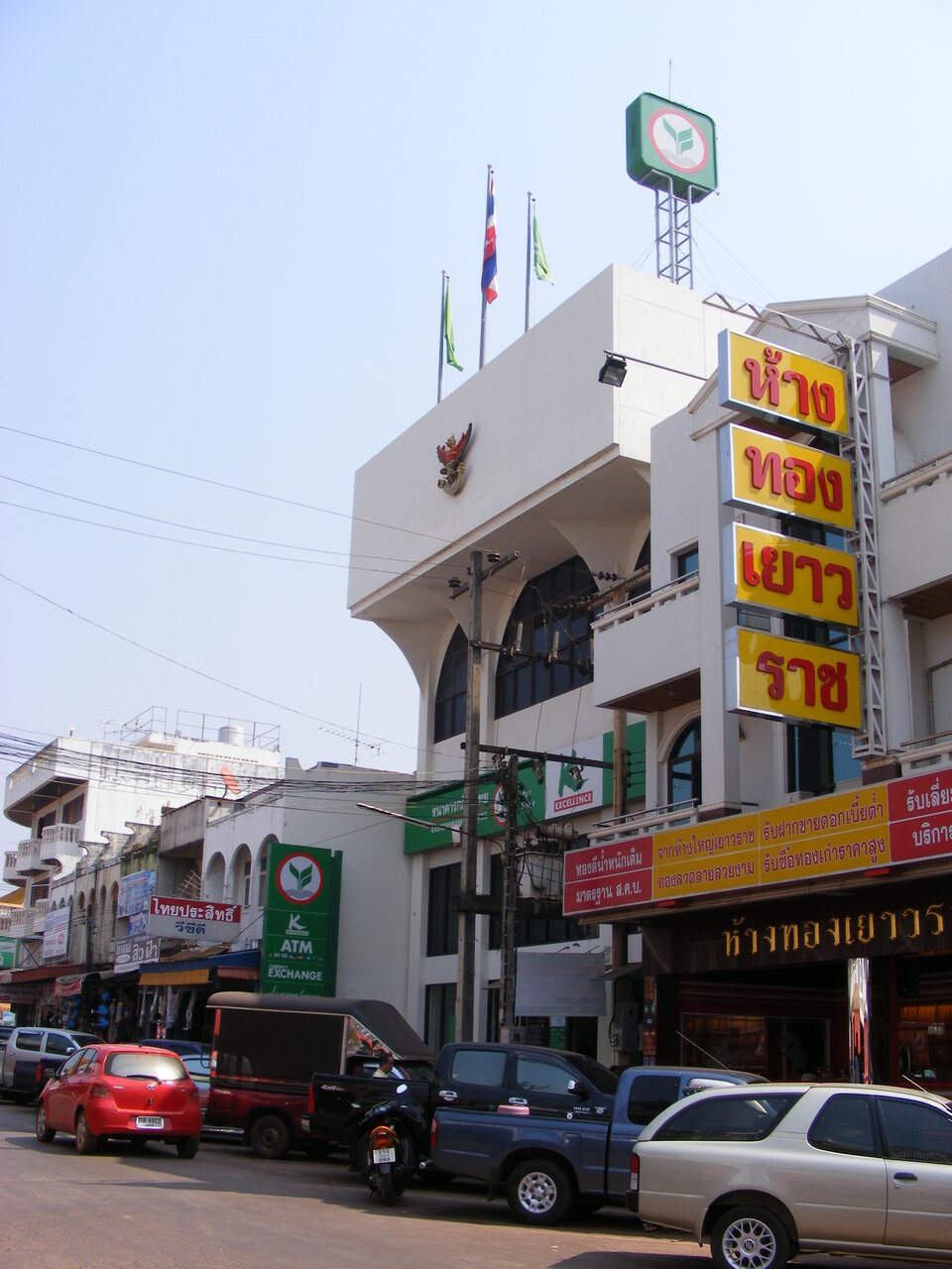 Kasikornbank branch in Ban Dung Udon Thani Thailand with a green ATM and currency exchange sign beside a Thai gold shop with red and yellow Thai script banners