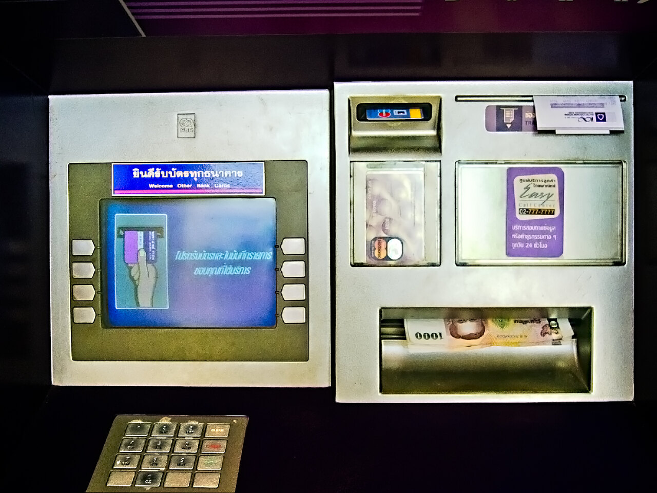 Close-up of a Thai ATM screen in Thailand showing Thai script reading yindi rap bat thuk thanakhan with 1000 baht notes in the cash slot