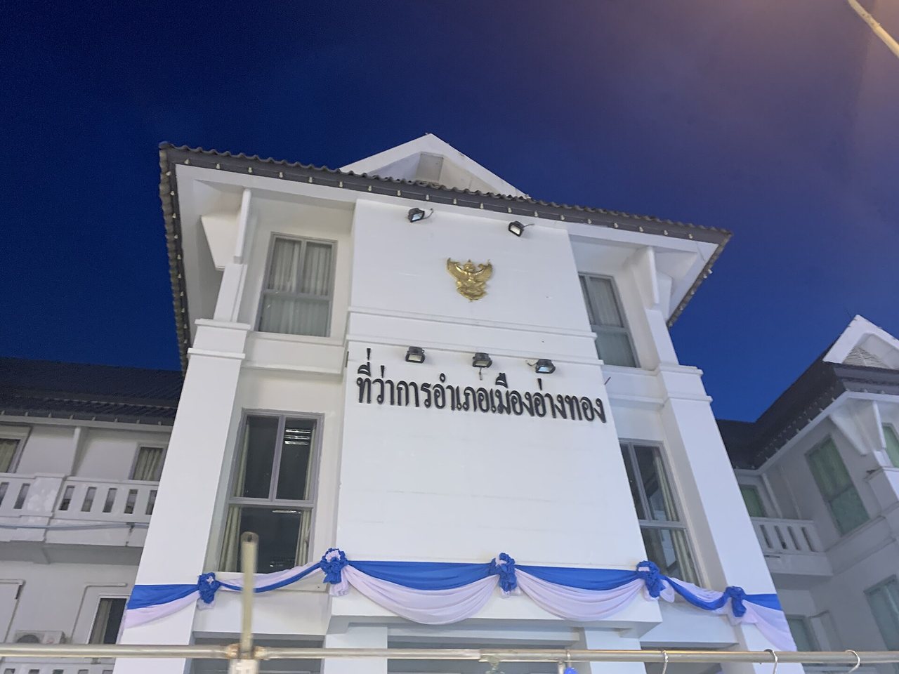 Mueang Ang Thong district office building in Thailand lit at dusk with Thai script reading thi wa kan amphoe Mueang Ang Thong