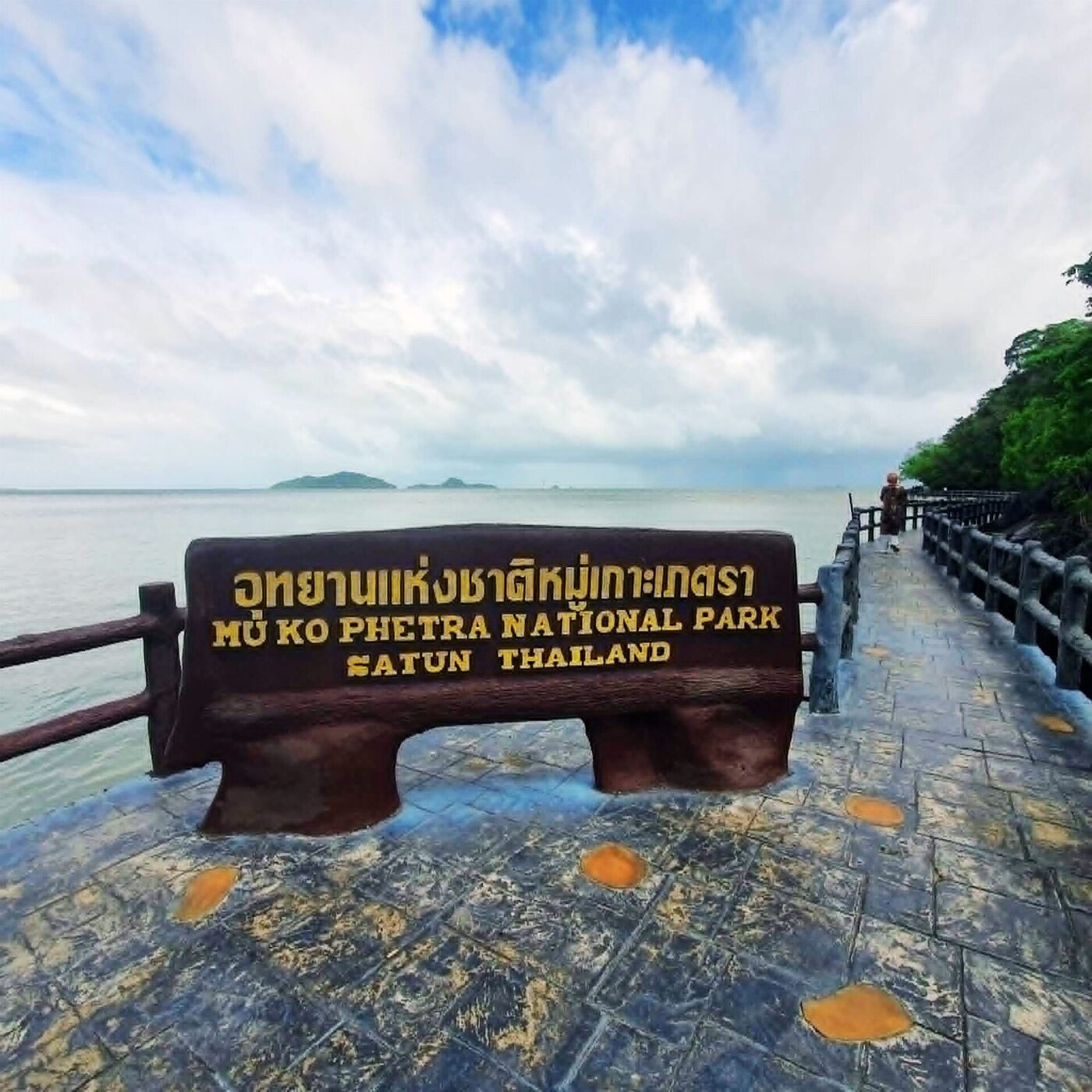 Wooden Mu Ko Phetra National Park sign in Satun Thailand with Thai script above the English park name beside the sea
