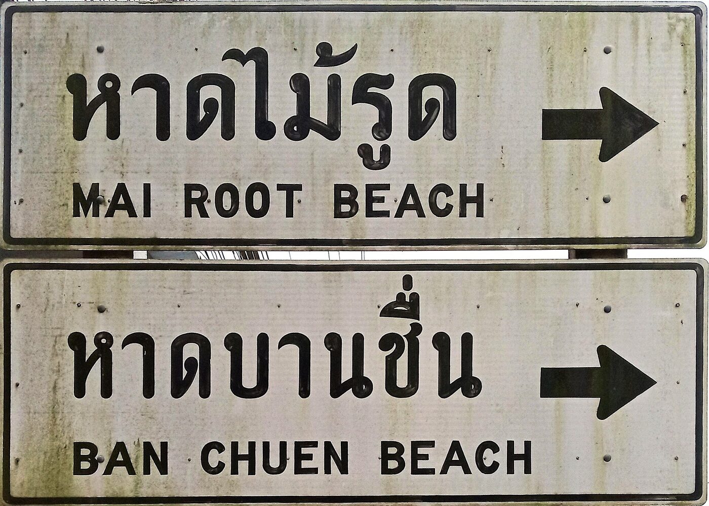 Bilingual Thai road sign in Trat Thailand reading Hat Mai Root and Hat Ban Chuen in Thai script with English beach names underneath