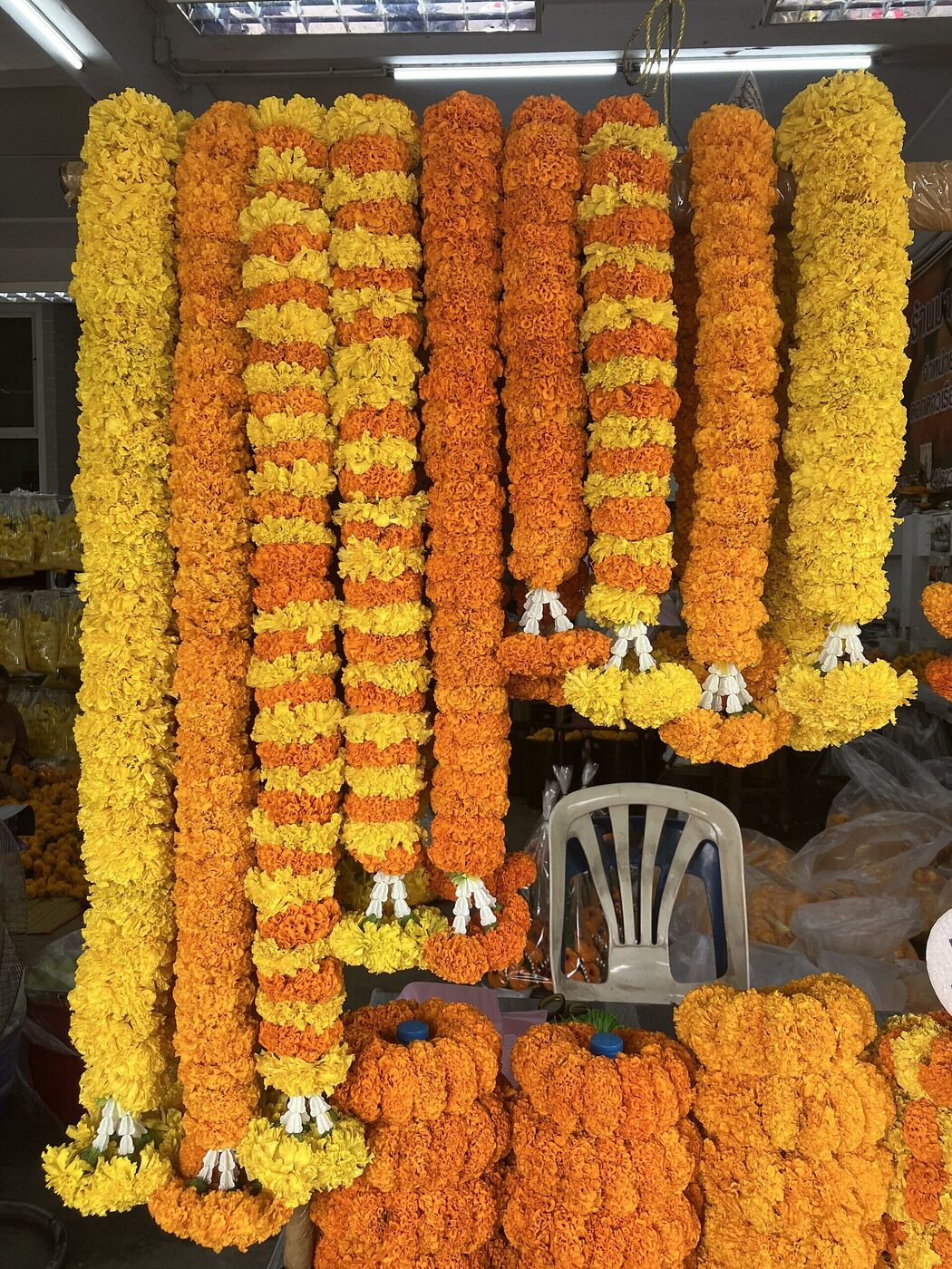 Long marigold and jasmine phuang malai garlands hanging for sale at Pak Khlong Talat flower market in Bangkok Thailand