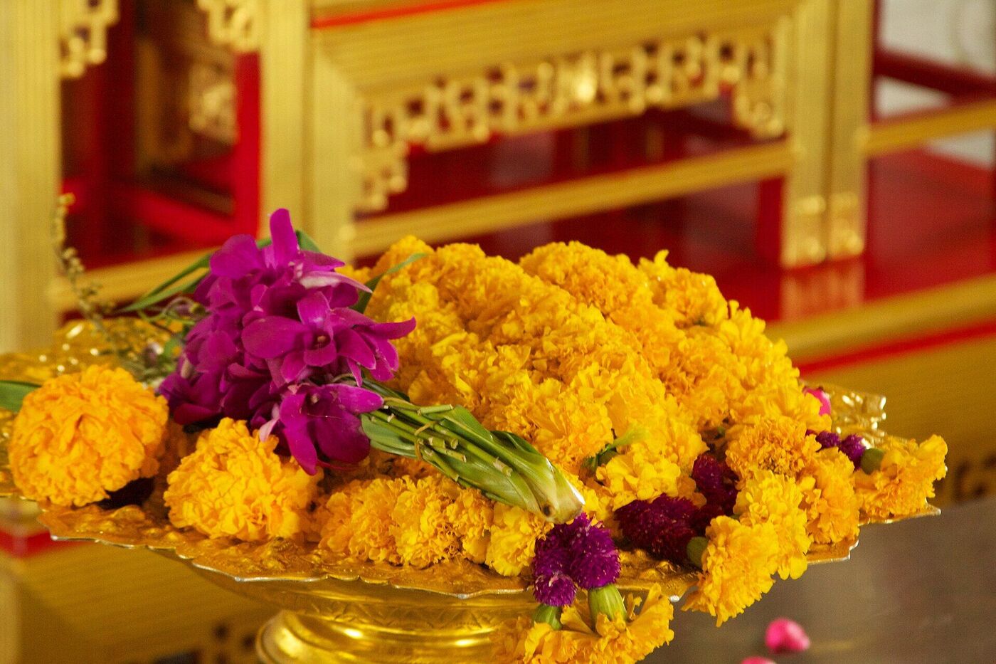 Gold tray of marigold and purple orchid offerings on an altar at Wat Traimit temple in Bangkok Thailand