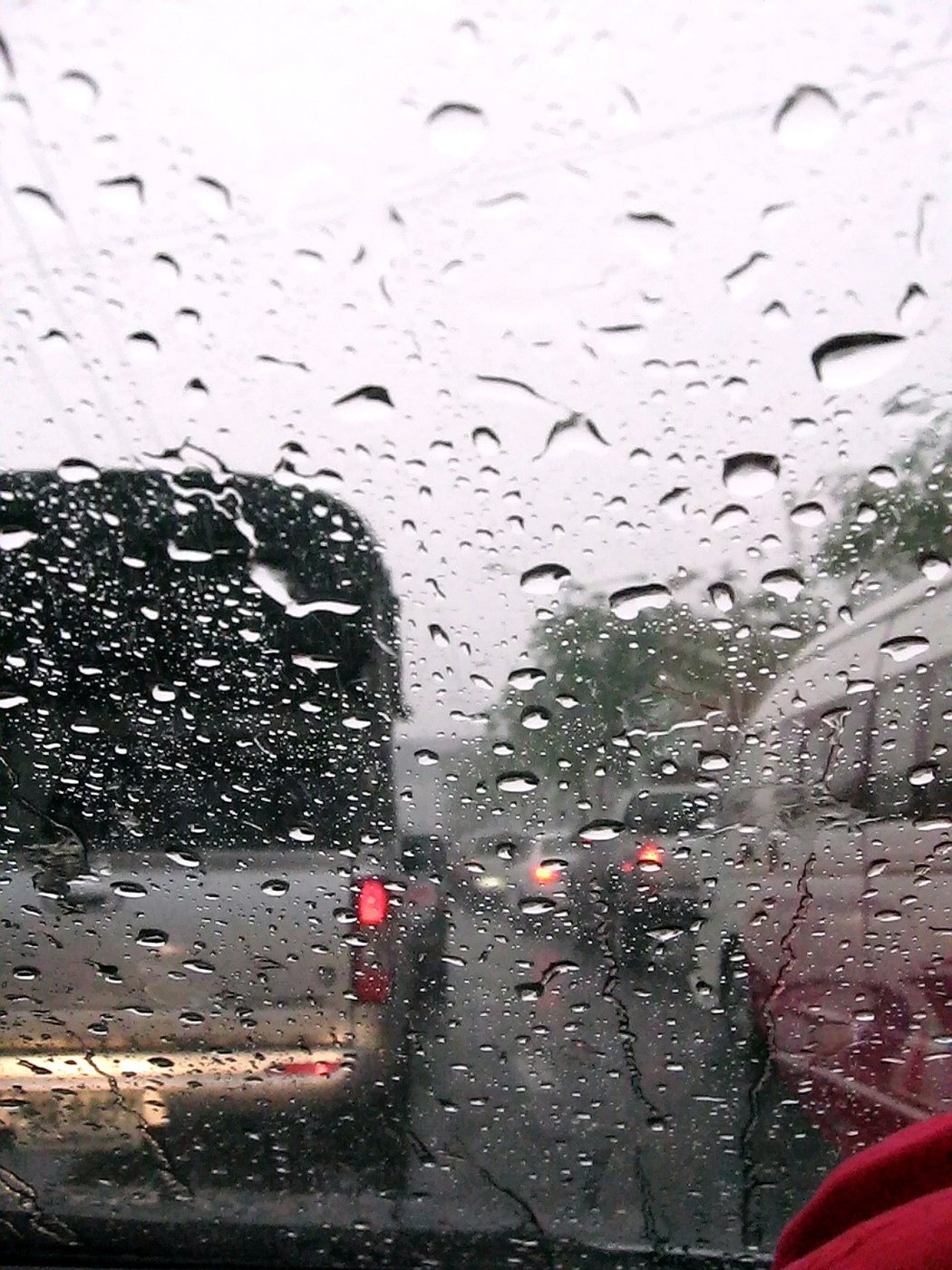 Heavy rain on a car windscreen during a Bangkok traffic jam in Thailand with red brake lights, illustrating Thai vocabulary for rain and traffic
