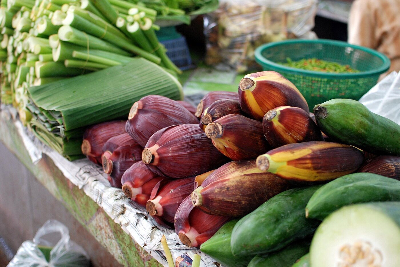 Purple banana flowers folded banana leaves and cucumbers for sale at Thanin market in Chiang Mai Thailand, a Thai vocabulary lesson in market produce