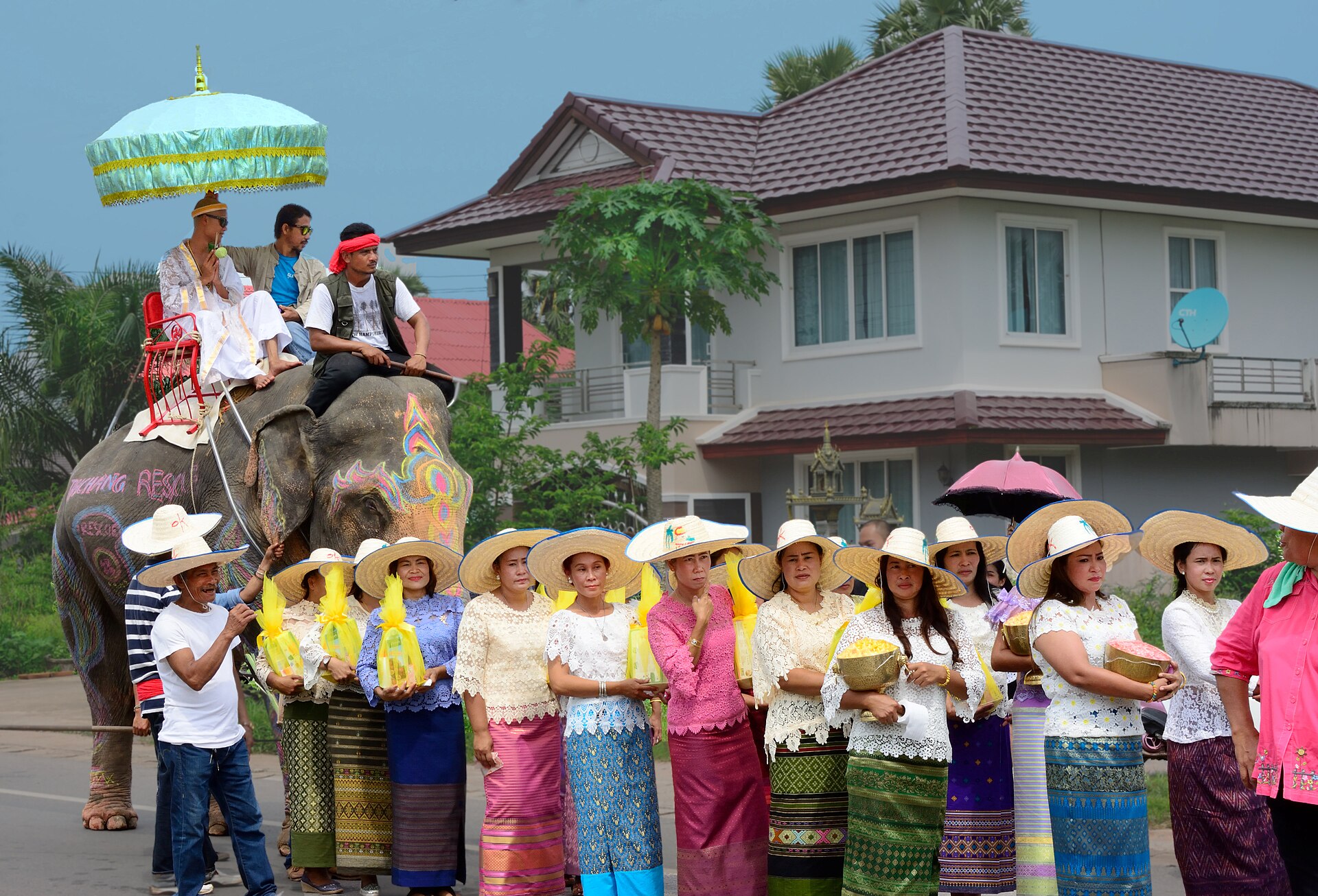 Thai wedding khan maak procession in a village with the groom riding an elephant and women in silk carrying offering trays in Thailand