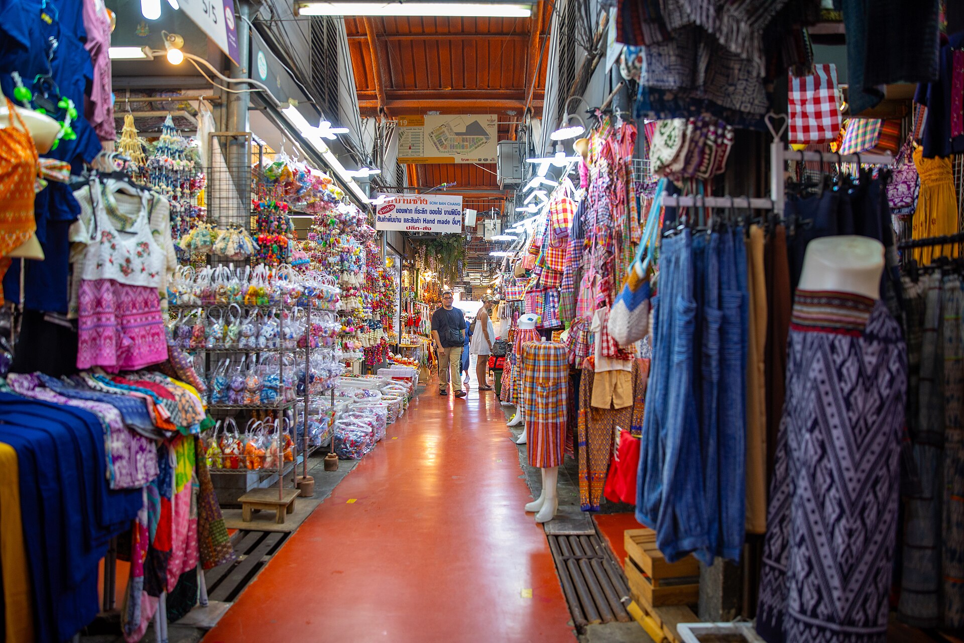Covered alley of clothing stalls hung with shirts, trousers and bags at Chatuchak Weekend Market in Bangkok, Thailand