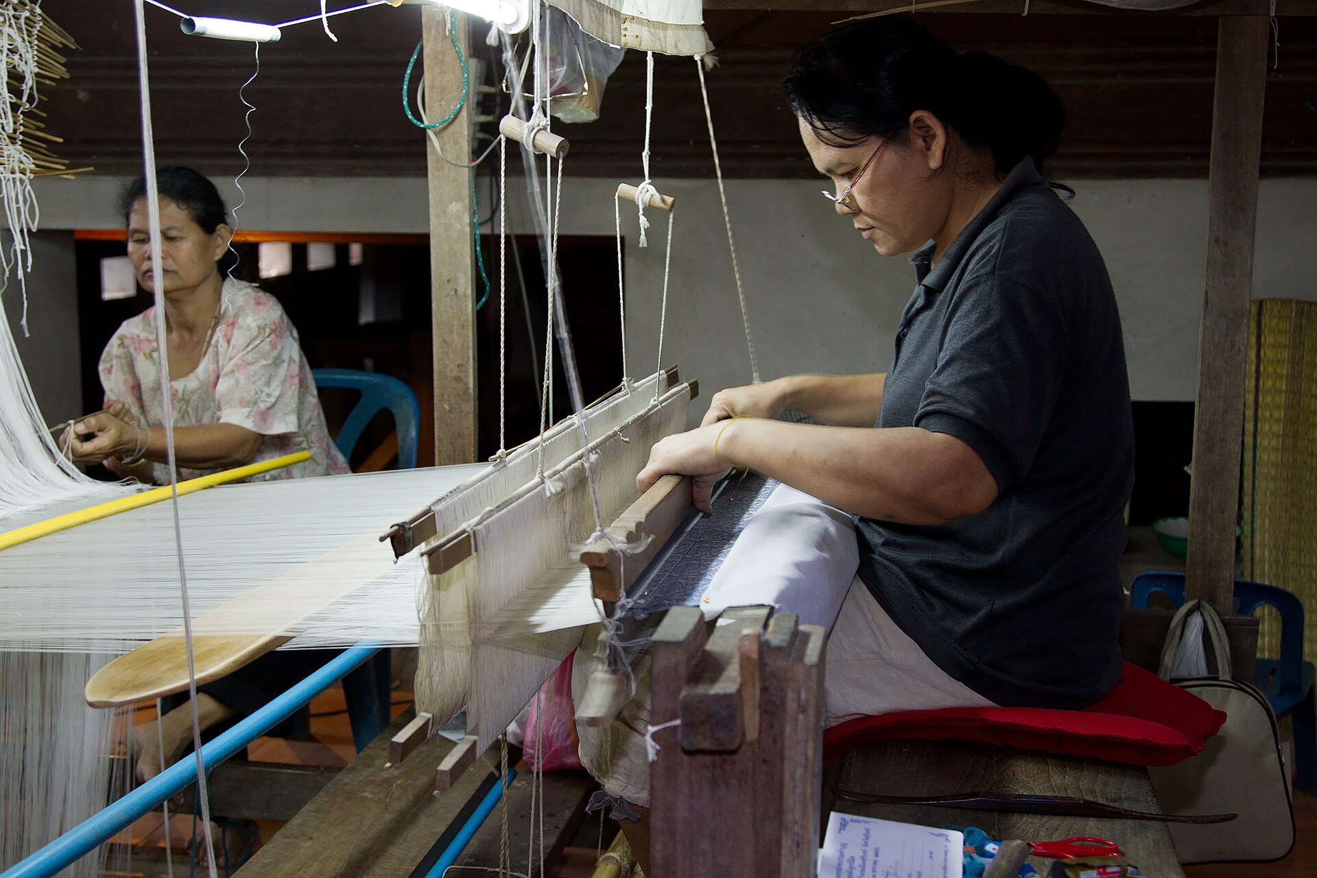 Two Thai women weaving silk thread on traditional wooden looms at Ban Tha Sawang in Surin province, Thailand