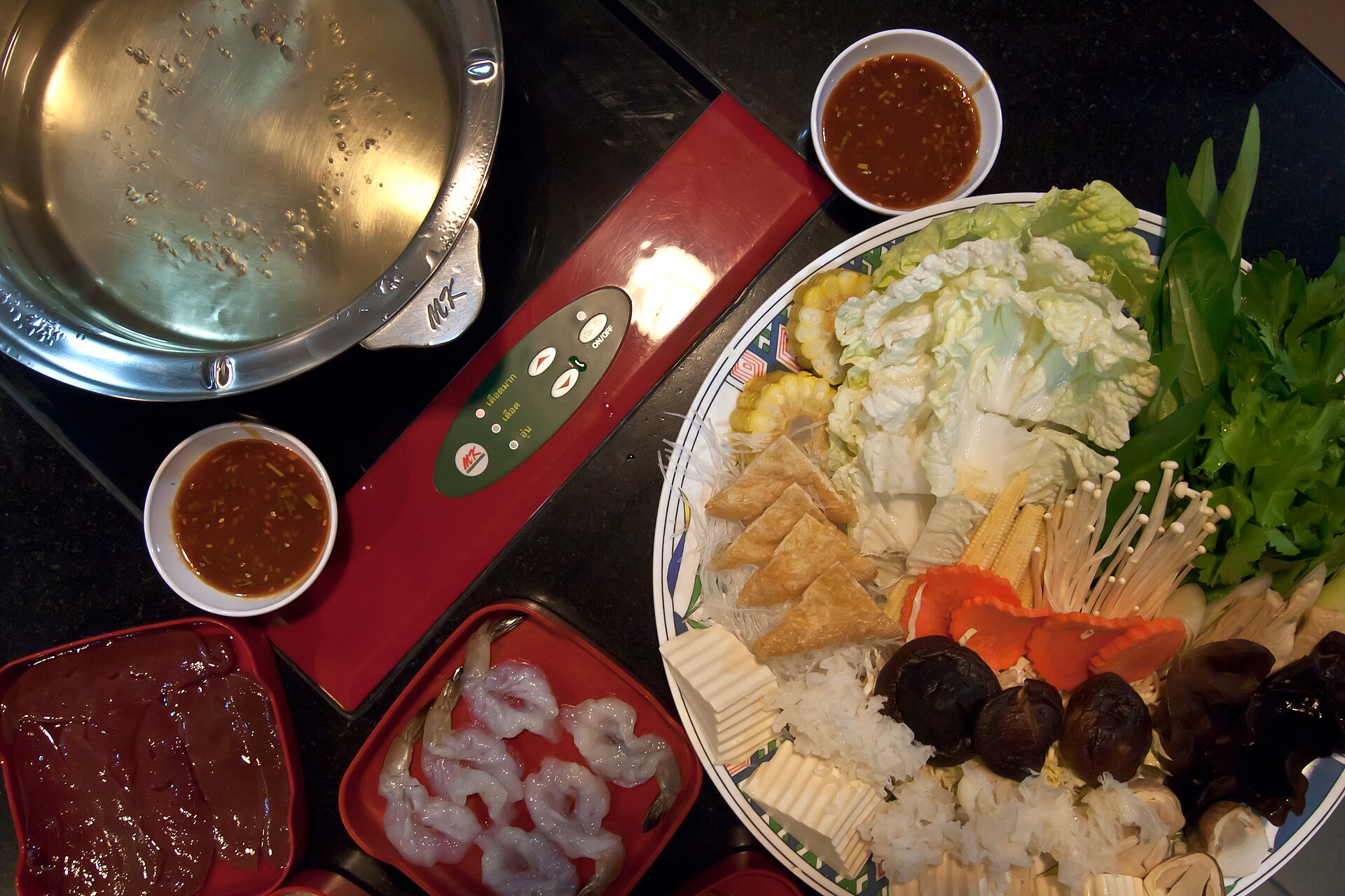 Thai suki hot pot set in Bangkok, Thailand with a platter of napa cabbage, enoki mushrooms, tofu and glass noodles beside bowls of red suki dipping sauce