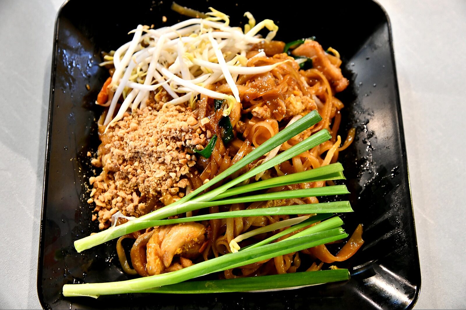 Plate of pad thai stir-fried rice noodles with chicken, bean sprouts, crushed peanuts and garlic chives served in Bangkok, Thailand