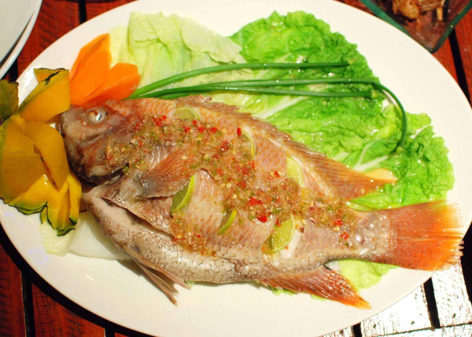 Whole steamed tilapia pla nueng manao topped with chilli garlic and lime sauce, served with lettuce and carved vegetables in Thailand