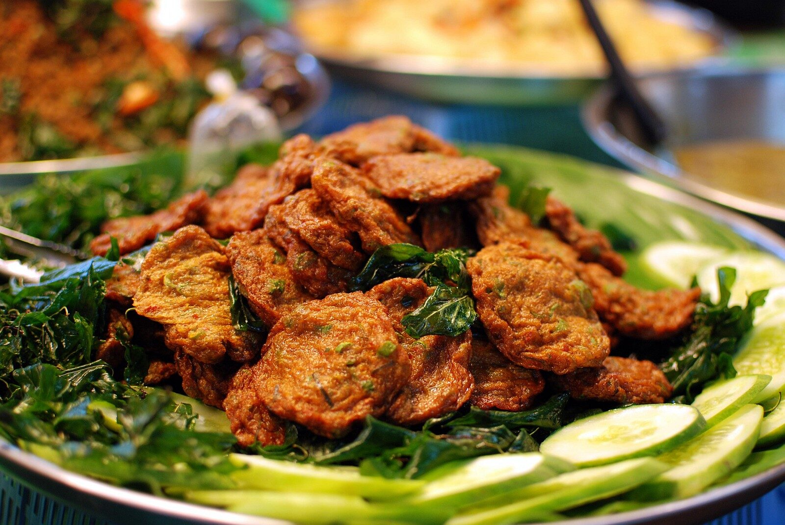 Heap of deep-fried Thai fish cakes thot man pla on fried holy basil leaves with sliced cucumber at Thanin market, Chiang Mai, Thailand