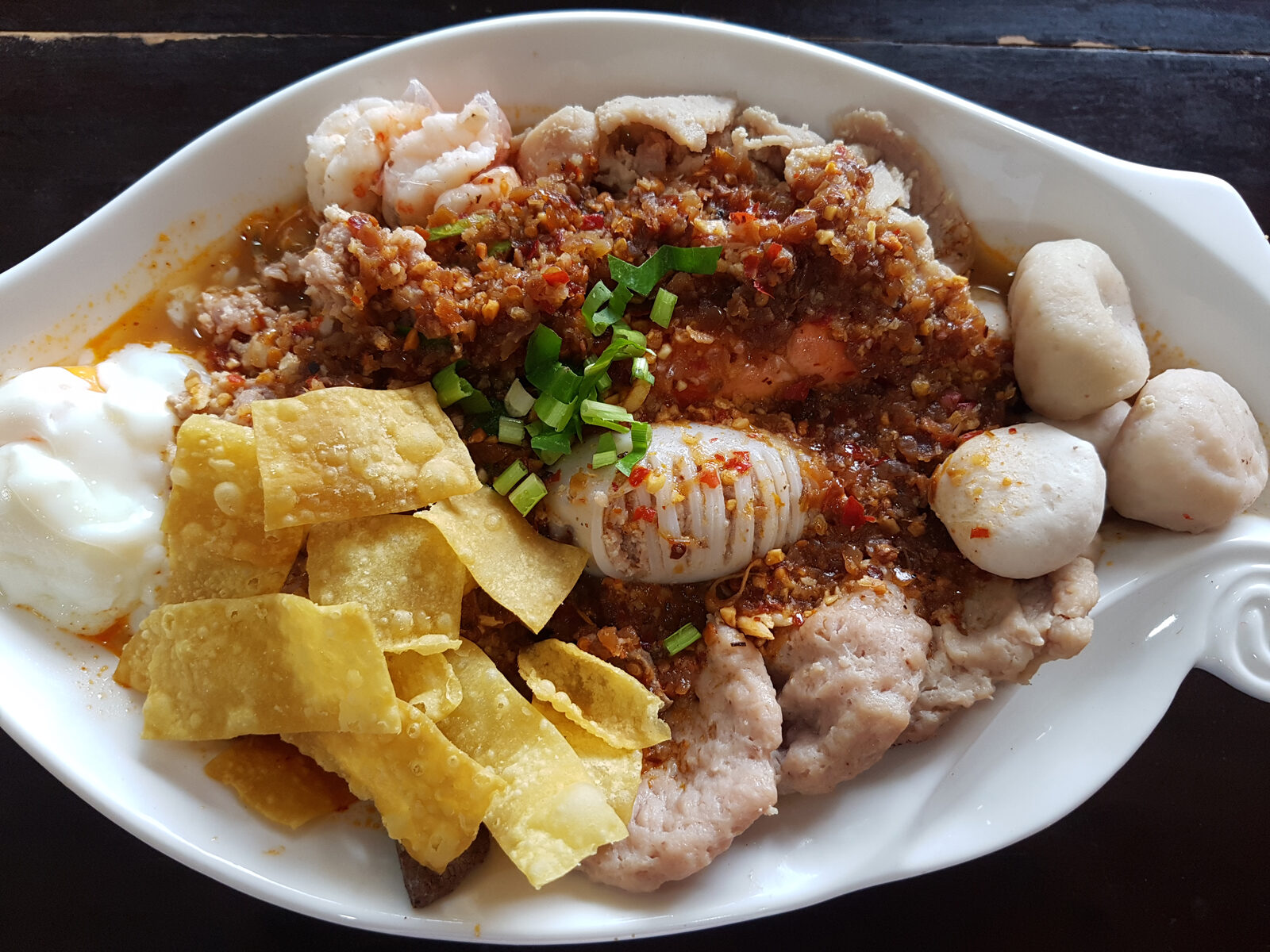 Bowl of Thai tom yam noodles in Bangkok, Thailand with prawns, minced pork, fish balls, squid, crispy wonton strips and a poached egg
