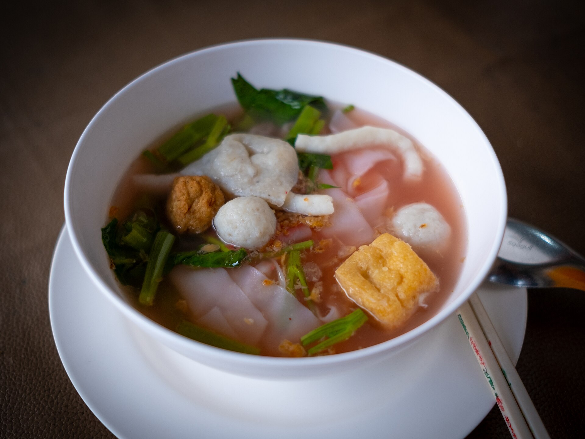White bowl of Thai yen ta fo pink noodle soup with wide rice noodles, fish balls, fried tofu, squid and morning glory